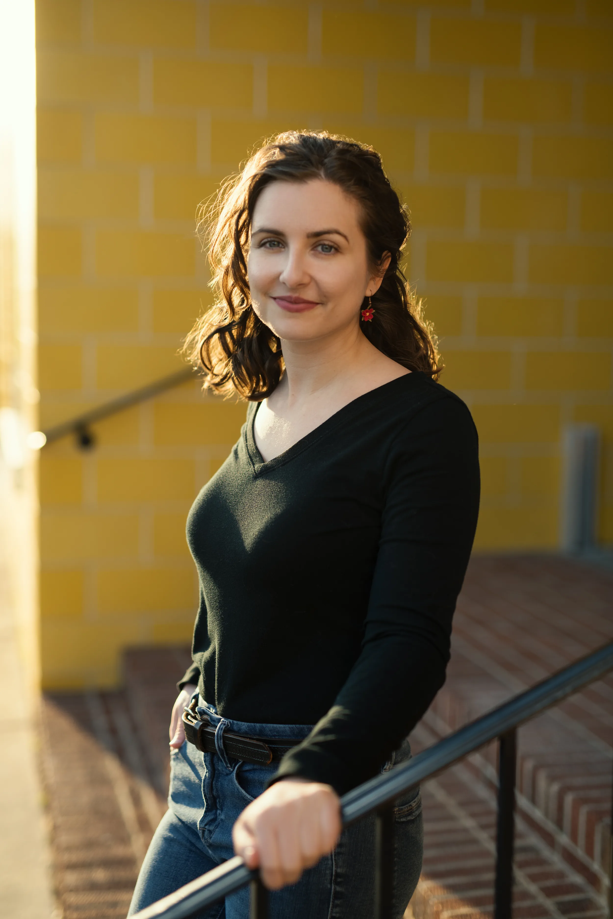 Dr. Renae DeLucia in a black top, smiling, on brick steps in front of a sunlit yellow wall